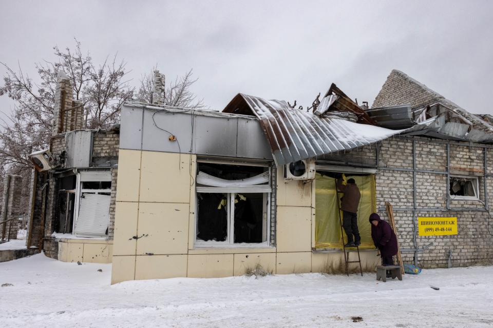 A man uses plastic sheets to cover a window of a building damaged by fighting in the frontline town of Lyman (REUTERS)