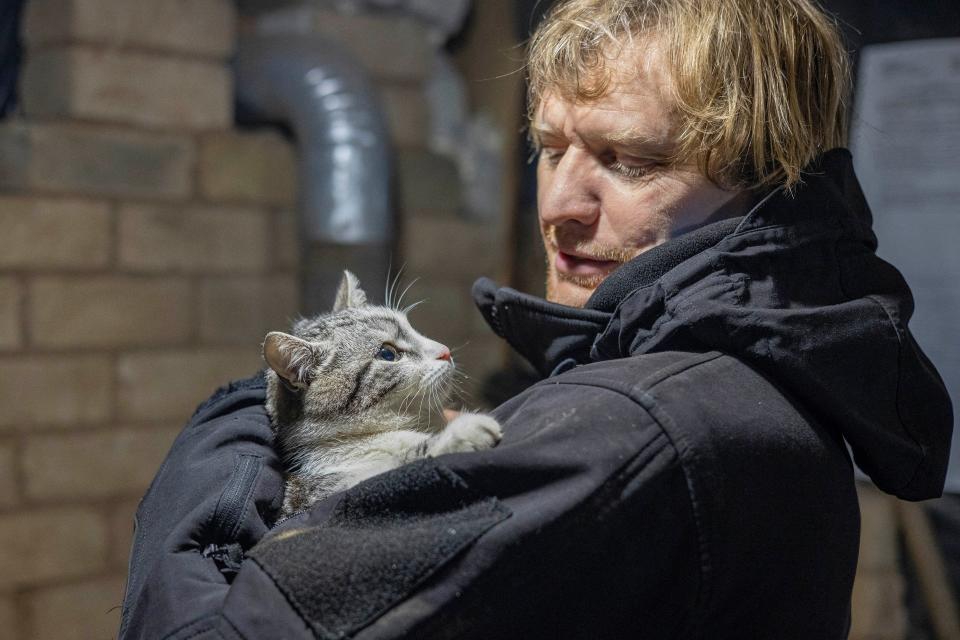 A man looks down at a cat he is holding in his arms.