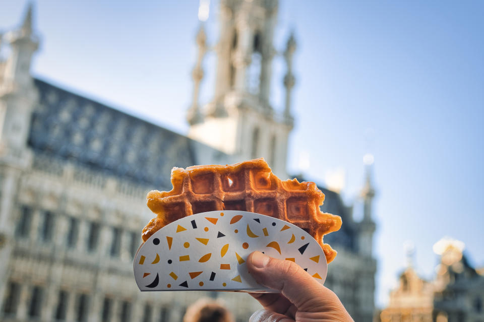 A hand holding a waffle against the background of the Grand Place in Brussels