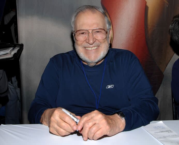 John Romita sits at a table smiling with a pen in his hand