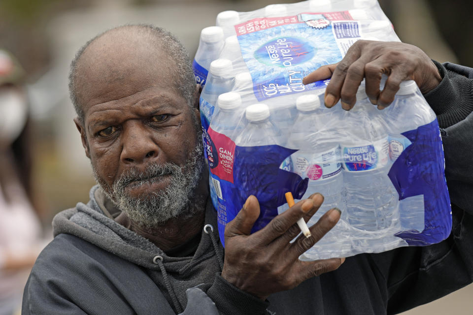 Kenneth Henderson carries a case of donated water back to his home, which was without running water after the recent winter storm, Friday, Feb. 26, 2021, in Houston. Local officials, including Houston Mayor Sylvester Turner, say they have focused their efforts during the different disasters on helping the underserved and under-resourced but that their work is far from complete. (AP Photo/David J. Phillip)