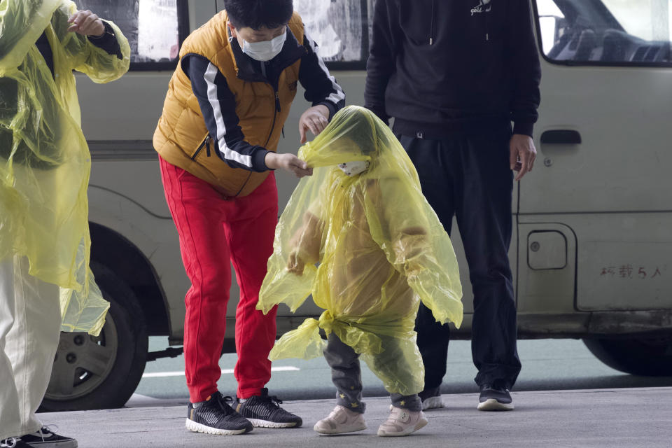 A woman wearing a face mask to protect against the spread of coronavirus puts a poncho on a child at Wuhan Tianhe International Airport in Wuhan (Ng Han Guan/AP)