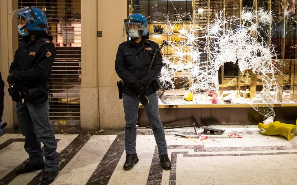 Police officers stand guard outside a Gucci boutique store as protesters gather during an anti government demonstration in Turin - Getty