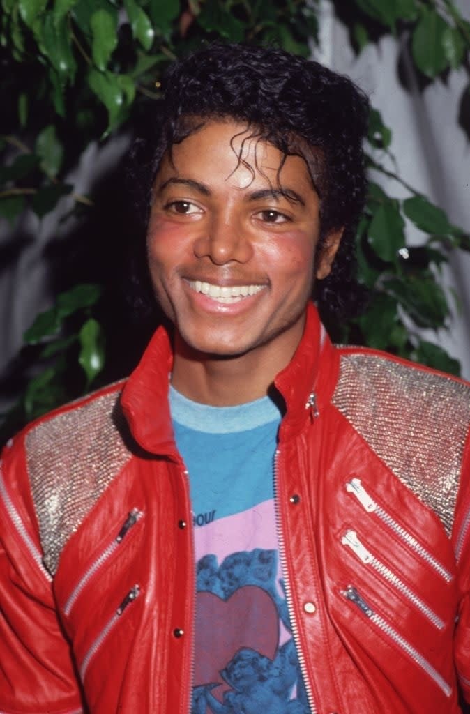 Michael Jackson wearing a red jacket with zippers and a graphic t-shirt, smiling