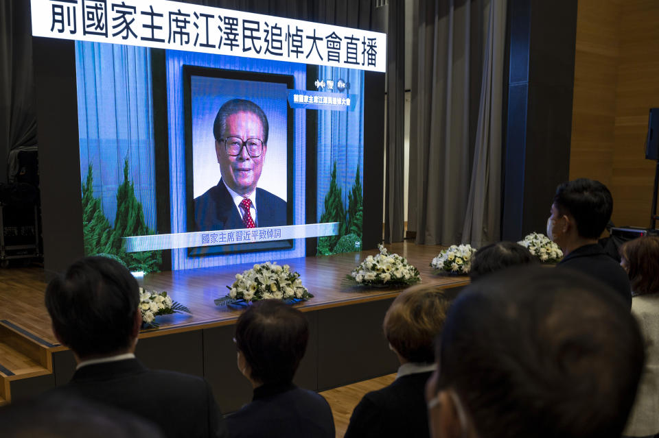 Residents watch a live broadcast of the memorial service for late former Chinese President Jiang Zemin on a screen at a community center in Hong Kong, Tuesday, Dec. 6, 2022. A formal memorial service was held Tuesday at the Great Hall of the People, the seat of the ceremonial legislature in the center of Beijing. Words on screen read "Former Chairman Jiang Zemin memorial live broadcast." (AP Photo/Vernon Yuen)