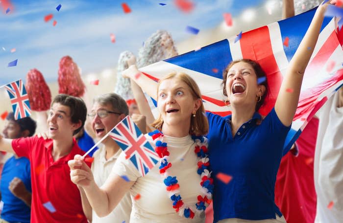 Group of excited fans with British flags cheering, one wearing a lei, in a festive atmosphere
