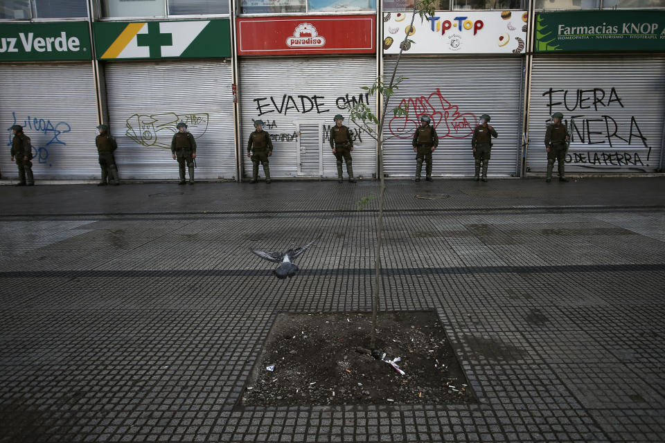 Police stand guard outside closed stores as a state of emergency remains in effect in Santiago, Chile, Sunday, Oct. 20, 2019. Protests in the country have spilled over into a new day, even after President Sebastian Pinera cancelled the subway fare hike that prompted massive and violent demonstrations. (AP Photo/Luis Hidalgo)