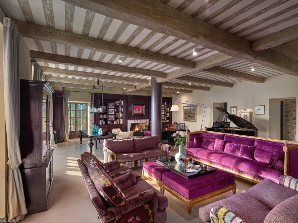 Luxurious living room with purple couches, a grand piano and fireplace. There are multiple pieces of art dotted around the room.