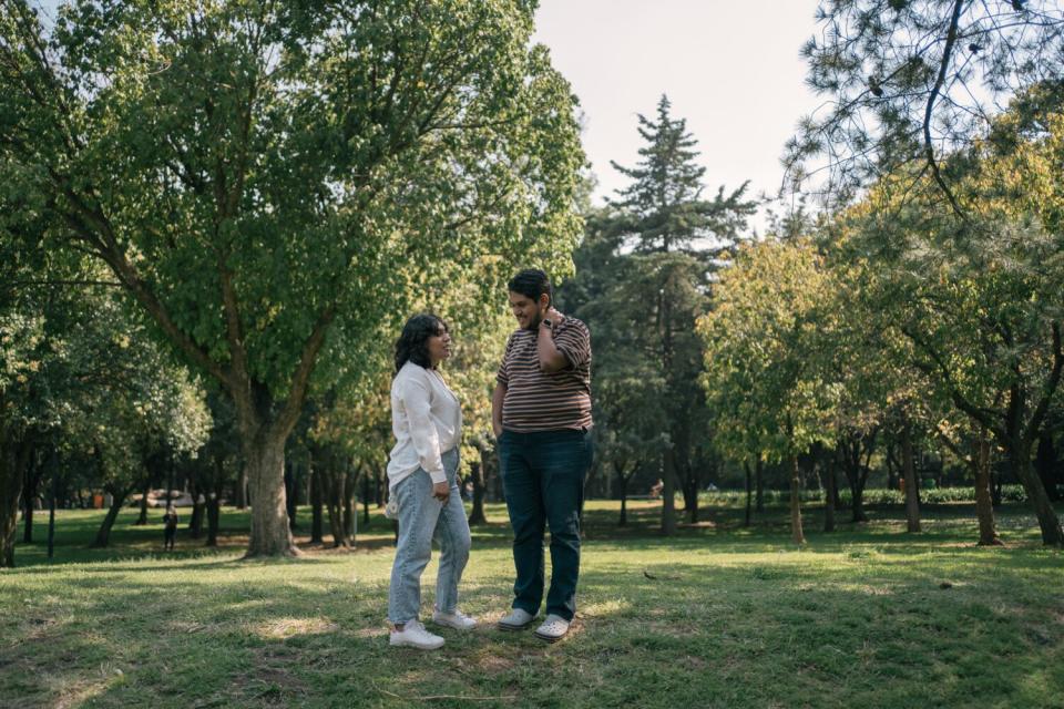 Two people standing on a grassy area with trees in the background