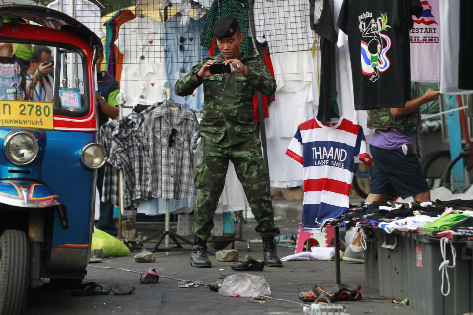 A soldier photographs the scene of an explosion littered with blood and small pairs of shoes at a main protest site in Bangkok, Thailand, Sunday, Feb. 23, 2014. More than a dozen people were hurt Sunday by a small explosion at an anti-government protest in Bangkok, less than a day after a bloodier attack in an eastern province killed one child and left about three dozen people wounded. (AP Photo/Wally Santana)