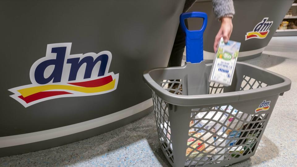 Eine Person legt in einer Filiale der Drogeriemarktkette dm im Kassenbereich ein Produkt in einen Einkaufskorb.