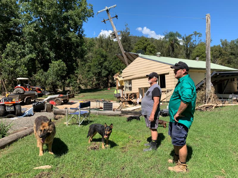 Australia cattle farmer Robert Costigan and his father-in-law Brian Watt stand in front of Watt's home that got swept off its foundations by floodwater and into a telegraph pole on the property in Hollisdale, Australia