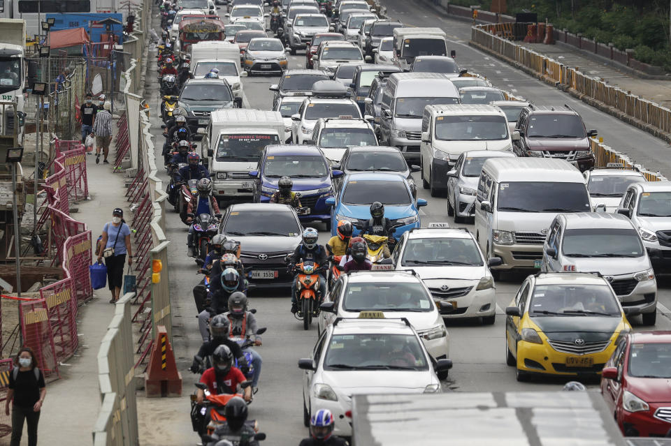 A woman wearing a face mask to prevent the spread of the coronavirus walks as traffic snarls in Quezon City, Philippines on Monday, Feb. 15, 2021. The Philippine government's approval for reopening many movie theaters, video game arcades and other leisure businesses closed since last year was postponed at least another two weeks after mayors feared it will bring new coronavirus infections. (AP Photo/Aaron Favila)