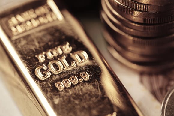 A gold bar lies next to a stack of gold coins.