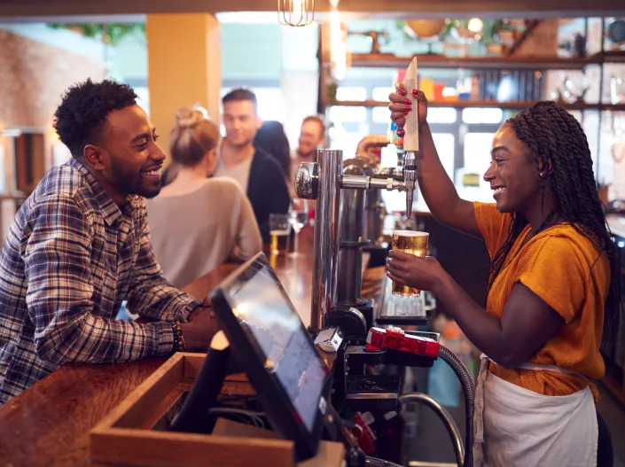 a bartender pouring a drink on tap at a bar for a smiling customer