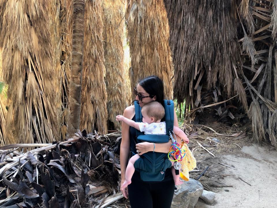 A woman and her baby next to large palm trees.