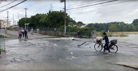 People stand at a flooded road damaged after an earthquake hit Osaka, Japan June 18, 2018, in this still image taken from a video obtained from social media. MANDATORY CREDIT. Twitter/@tw_hds/via REUTERS