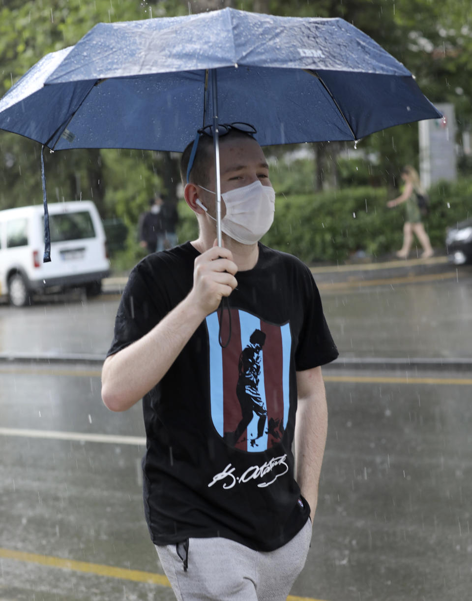 A man wearing a face mask to protect against the spread of coronavirus, walks in rain in a popular street, in Ankara, Turkey, Wednesday, June 17, 2020. Turkey has made the wearing of face masks mandatory in five more provinces, following an uptick in COVID-19 cases. Health Minister Fahrettin Koca tweeted Tuesday that the wearing of masks is now compulsory in 42 of Turkey's 81 provinces.(AP Photo/Burhan Ozbilici)