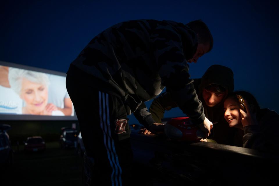 The advertisements begin at Holiday Drive-In in Reo, Ind., as Aiden Roberts, 16, top, tries to help his friends, James Evans, 15, and Taylor Sharp, 16, with their portable radio to hear the movie "Trolls World Tour" Friday evening, May 8, 2020. It was the opening night for the drive-in celebrating its 65th year in operation. With the COVID-19 pandemic regulations relaxing, the drive-in had a good crowd despite the chilly temperatures and brisk wind.