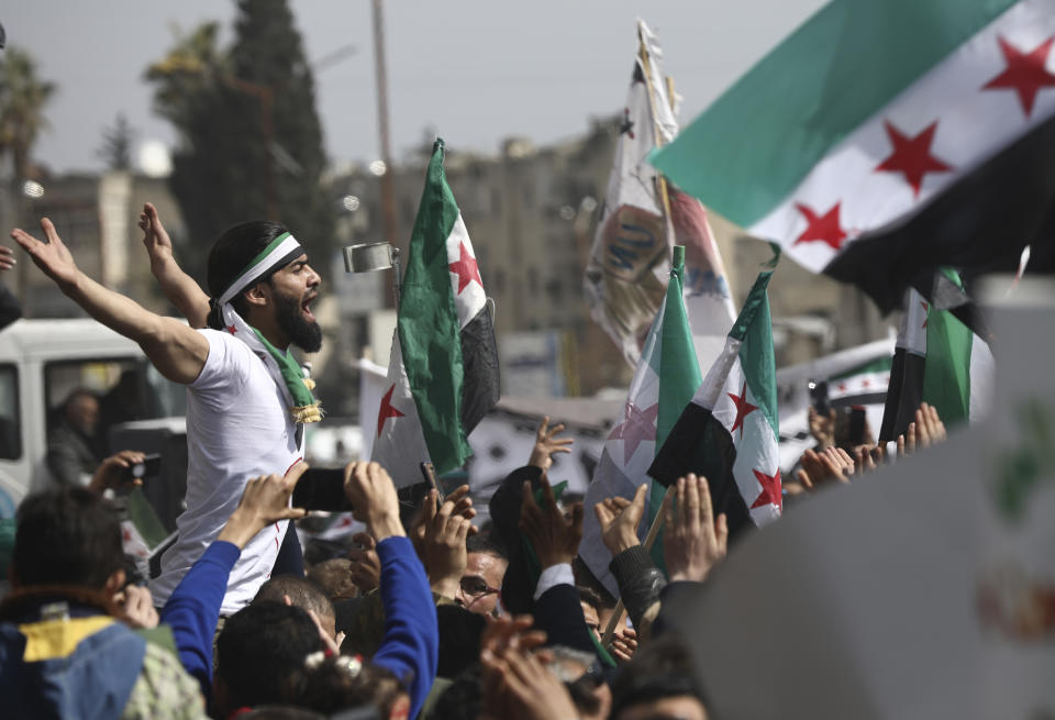 An anti-Syrian government protester shouts slogans as others wave revolutionary flags, to mark 10 years since the start of a popular uprising against President Bashar Assad's rule, that later turned into an insurgency and civil war, In Idlib, the last major opposition-held area of the country, in northwest Syria, Monday, March 15, 2021. (AP Photo/Ghaith Alsayed)