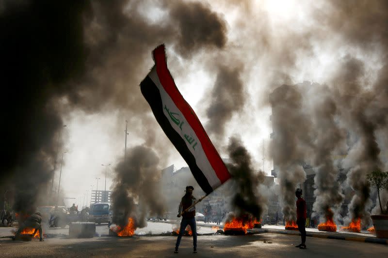 FILE PHOTO: A protester holds an Iraqi flag amid a cloud of smoke from burning tires during ongoing anti-government protests in Najaf