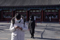 A man wearing a face mask to help curb the spread of the coronavirus browses his smartphone as a masked security guard stands near the quiet ticket counters at the Forbidden City in Beijing, Sunday, Jan. 10, 2021. More than 360 people have tested positive in a growing COVID-19 outbreak south of Beijing in neighboring Hebei province. (AP Photo/Andy Wong)