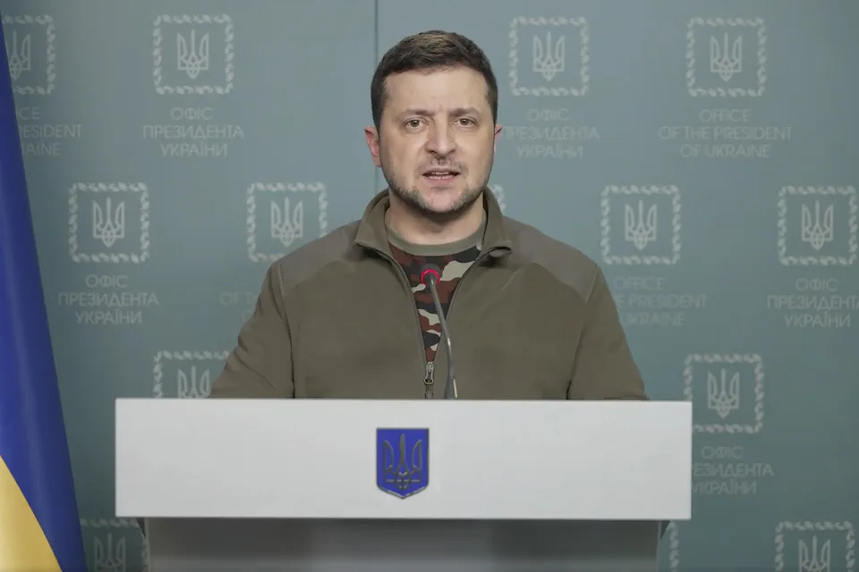 Ukrainian President Volodymyr Zelensky at a white podium with a blue embossed shield for Ukraine. 