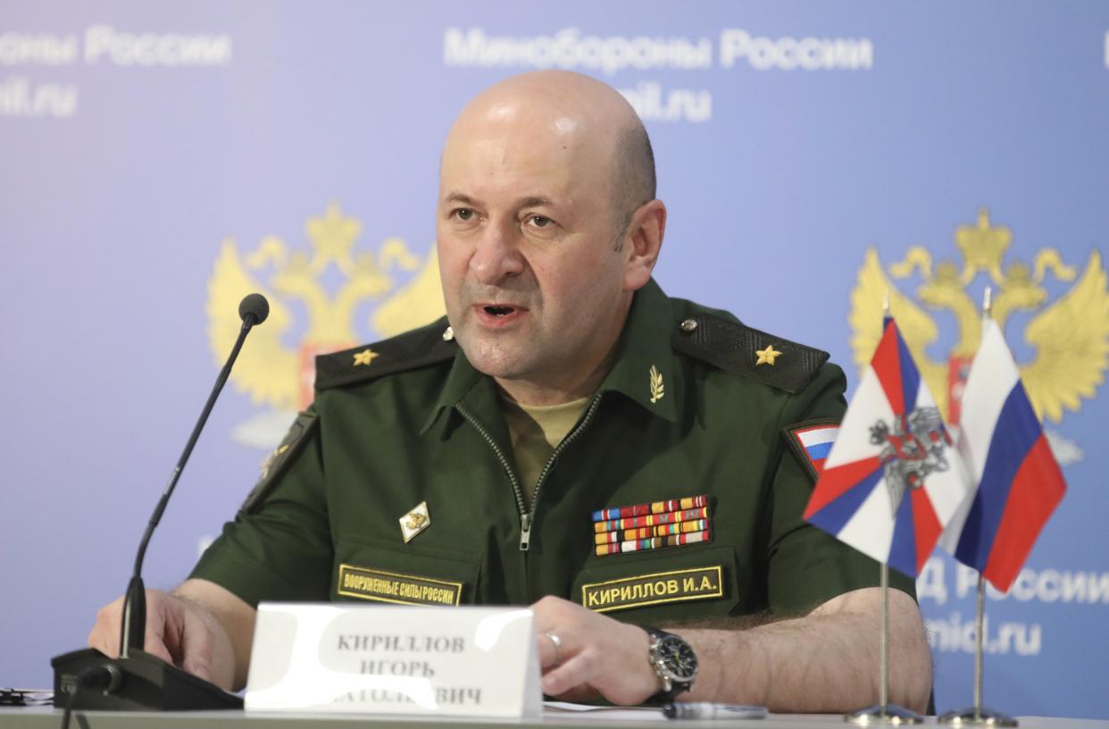 Lt. Gen. Igor Kirillov at the microphone, wearing a uniform showing his name and a row of military awards, and next to two small Russian flags.