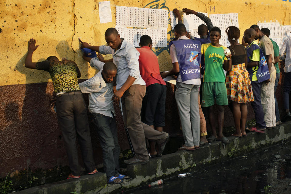 Election officials tape the voter's registrations list to the wall of the Les Anges primary school in Kinshasa, Congo, as voters start to check their names, Sunday Dec. 30, 2018. The voting process was delayed when angry voters burned six voting machines and ballots mid-day, angered by the fact that the registrations lists had not arrived. Replacement machines had to be brought in, and voting started at nightfall, 12 hours late. Forty million voters are registered for a presidential race plagued by years of delay and persistent rumors of lack of preparation. (AP Photo/Jerome Delay)