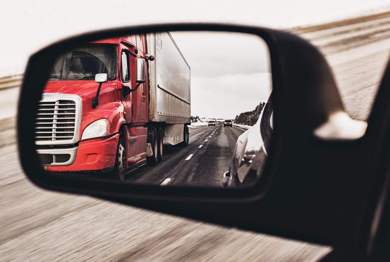 Semi truck in the side view mirror of a car.