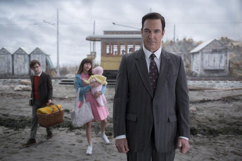 man standing in the foreground as three kids walk with their duffel bags in the background