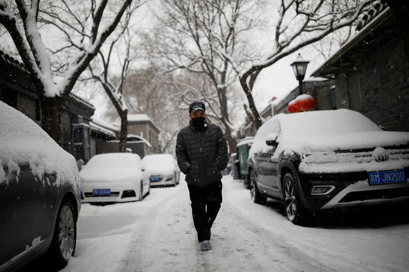 Man wearing a face mask walks past snow-covered vehicles as the country is hit by an outbreak of the novel coronavirus, in Beijing