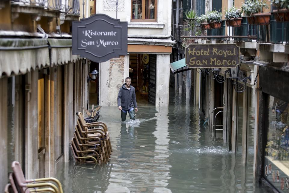 A ma makes his way through water in Venice, Italy, Friday, Nov. 15, 2019. Waters are rising in Venice where the tide is reaching exceptional levels just three days after the Italian lagoon city experienced its worst flooding in more than 50 years. (AP Photo/Luca Bruno)