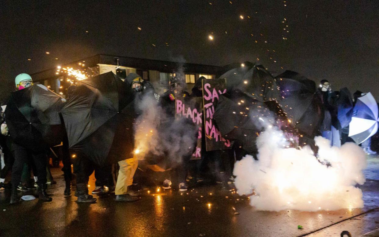 Demonstrators protect themselves with umbrellas against tear gas and pepper balls outside the Brooklyn Center police station - AFP