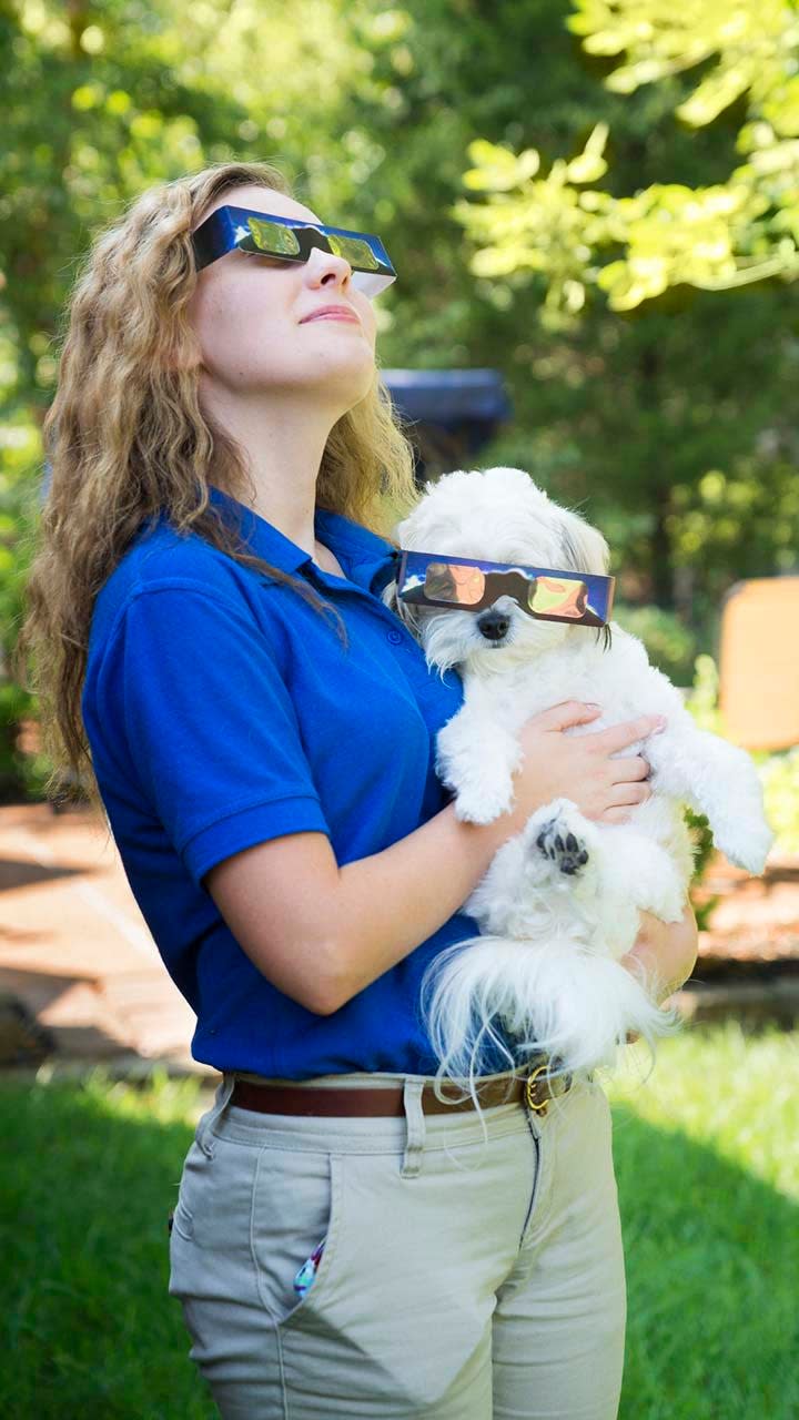 Pet owner and dog wearing solar eclipse viewing glasses