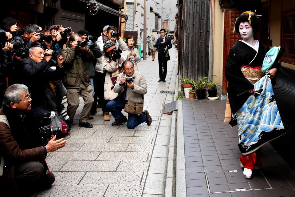 A maiko posing for photos in front of a crowd of people with cameras.