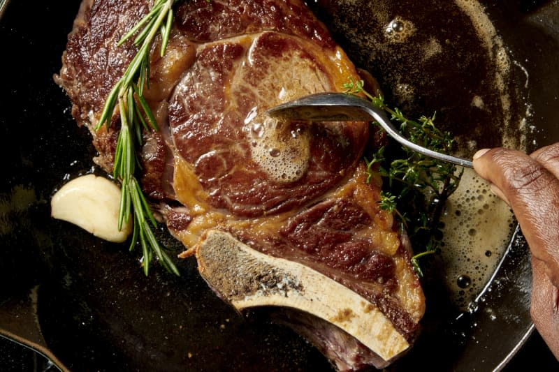 a seared steak being basted with garlic, rosemary, thyme, and butter in a cast iron skillet