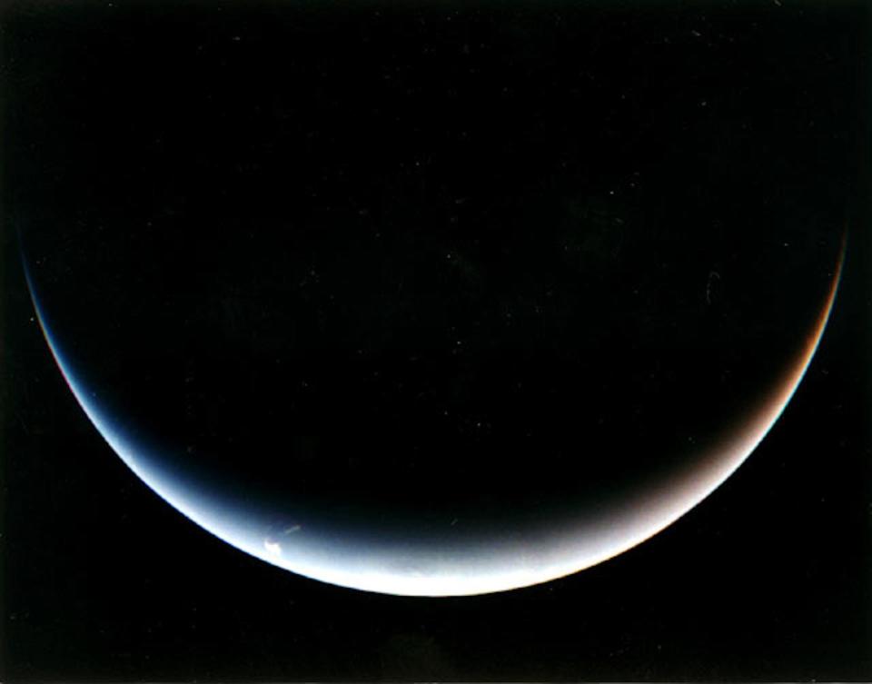 the crescent shape of Neptune south pole is seen by voyager as it departs.