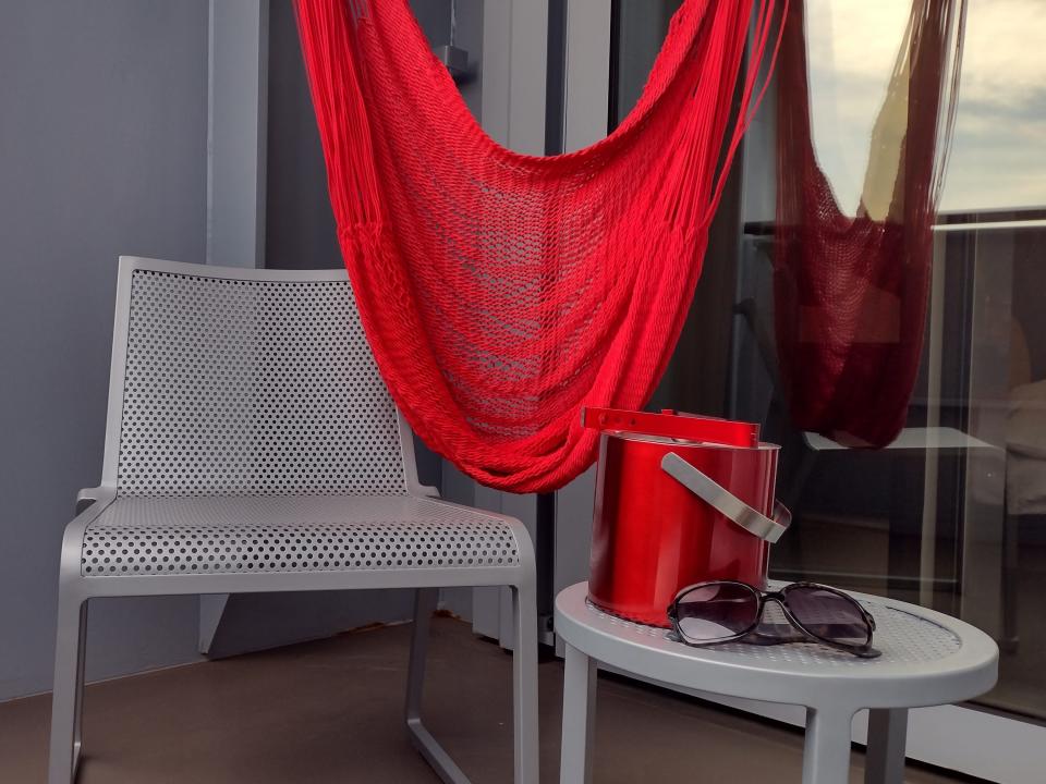A chair with a matching table and a red ice bucket and a draped hanging red hammock.