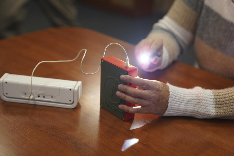 Minh Ha, assistive technology manager at the Perkins School for the Blind uses a flashlight to try a LightSound device, attached to an external speaker, for the first time at the school's library in Watertown, Mass., on March 2, 2024. Wanda Díaz-Merced, an astronomer who is blind, a co-creator of the device, says, “The sky belongs to everyone. And if this event is available to the rest of the world, it has to be available for the blind, too. ... I want students to be able to hear the eclipse, to hear the stars." (AP Photo/Mary Conlon)