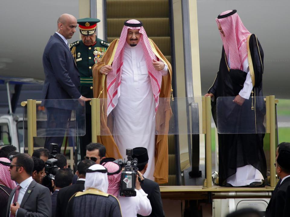 Saudi King Salman, center, adjusts his headscarf as he steps down the stairs of his plane upon arrival at Halim Perdanakusuma Airport in Jakarta, Indonesia, Wednesday, March 1, 2017. Salman arrived in the world's largest Muslim nation on Wednesday as a part of a multi-nation tour aimed at boosting economic ties with Asia.