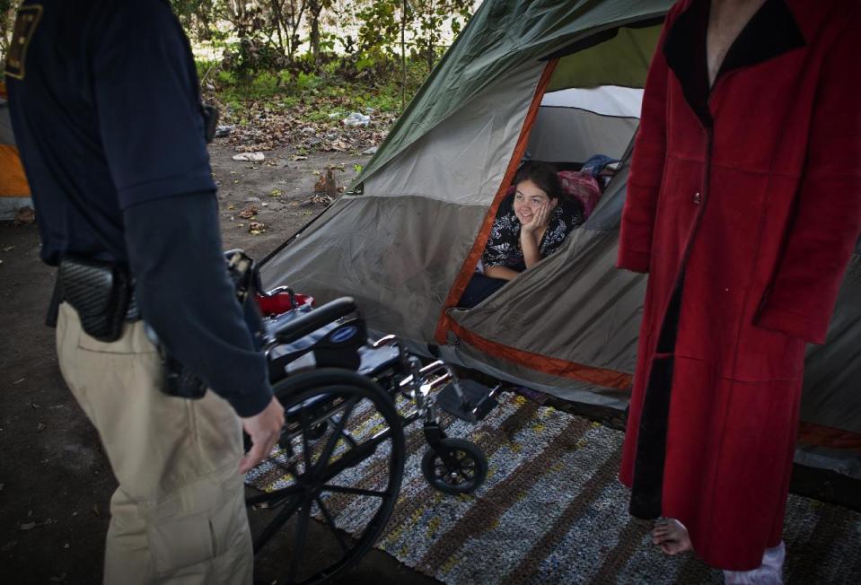 In this Friday, Dec. 13, 2013 photo, A young homeless woman known as "Crystal," center, thanks Homeless Liaison Officer Tom Gentner for her new wheelchair at Camp 8 South under the Truman Parkway in Savannah, Ga. Her previous wheelchair was damaged by rocks on a path to the camp, and he contacted Savannah Christian Church who found a used wheelchair for donation. (AP Photo/Stephen B. Morton)