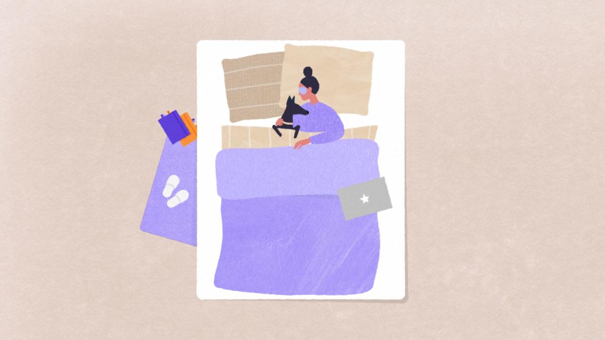 a person laying in bed under the covers, wearing an eye mask and cuddling a dog. on the floor beside the bed is a rug with shoes and notebooks on top of it. there's a laptop on the foot of the bed.