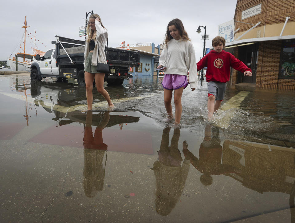 Madelyn Haeger, 17, left, of Palm Harbor, walks with Victoria Arena, 12, center, and Joshua Arena, 9, both from Kirkland, Wash., as they negotiate a flooded intersection along the Sponge Docks Thursday, April 11, 2024 in Tarpon Springs, Fla. (Chris Urso/Tampa Bay Times via AP)