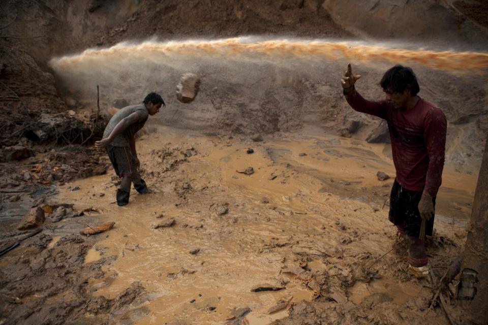 In this May 3, 2014 photo, a jet stream of water passes above two miners known as "Maraqueros" who remove stones and chunks of tree trunks that have been released with the aid of a rustic type of hydraulic jet known locally as a "Chupadera," in La Pampa in Peru's Madre de Dios region. The Chupadera aims powerful jet streams of water at earth walls, releasing the soils that hold the sought after flecks of gold. (AP Photo/Rodrigo Abd)