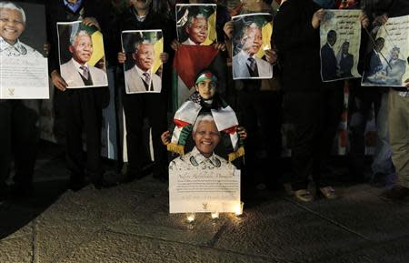Palestinians light candles and hold placards bearing images of former South African President Nelson Mandela outside the Church of Nativity in the West Bank town of Bethlehem December 7, 2013. REUTERS/Ammar Awad