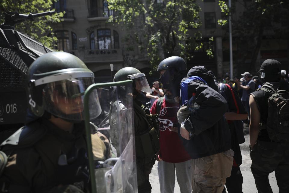 An anti-government protester defies riot police in Santiago, Chile, Tuesday, Oct. 22, 2019. The government said Tuesday that 15 people have died in five days of rioting, arson and violent clashes that were sparked by a hike in subway fares and have almost paralyzed the country. (AP Photo/Rodrigo Abd)