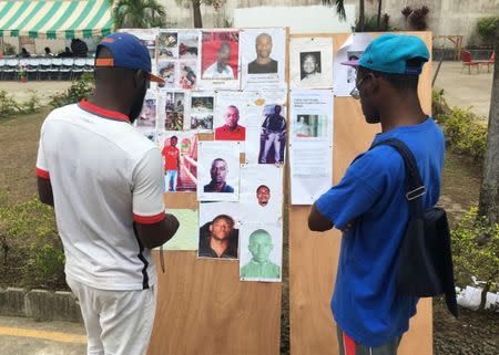 Men examine a poster board showing people who died or are still missing following clashes after elections in Libreville, Gabon, September 19, 2016. REUTERS/Edward McAllister