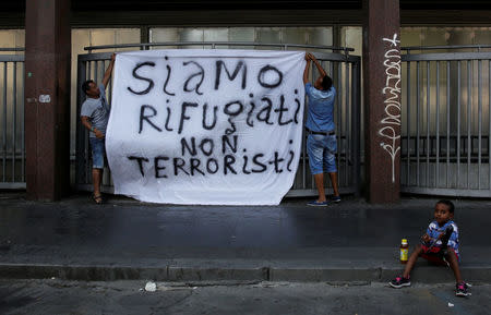 Refugees hang a banner reading "We are refugees, we aren't terrorists", after being forcibly removed from a building where they had been living, in central Rome, Italy, August 20, 2017. REUTERS/Alessandro Bianchi