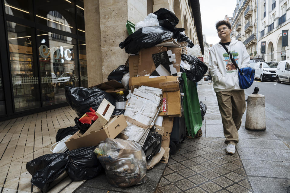 A man walks past uncollected garbage in Paris, Monday, March 13, 2023. A contentious bill that would raise the retirement age in France from 62 to 64 got a push forward with the Senate's adoption of the measure amid strikes, protests and uncollected garbage piling higher by the day. (AP Photo/Lewis Joly)